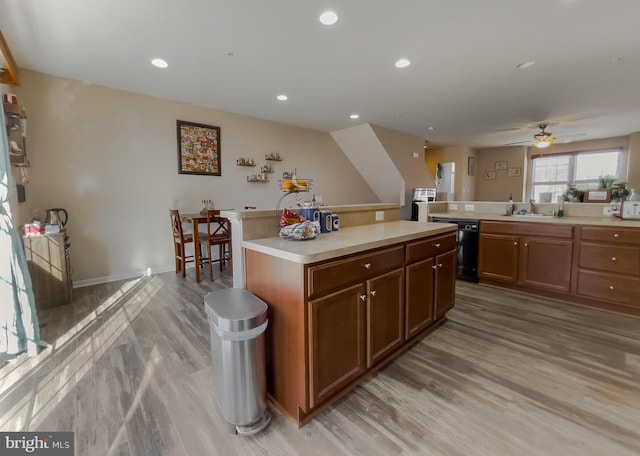 kitchen with light wood finished floors, dishwasher, a center island, light countertops, and a sink