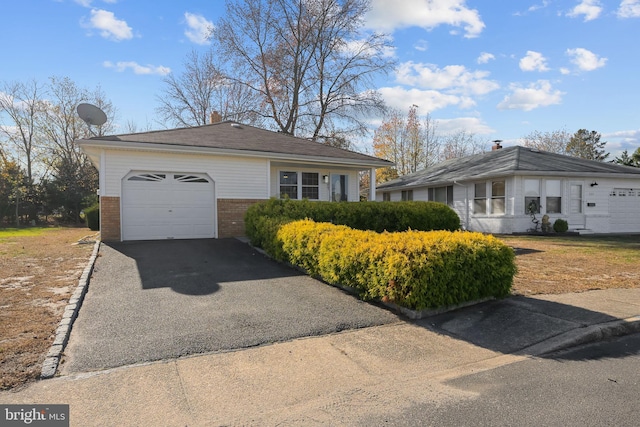 ranch-style home with a garage, brick siding, a chimney, and aphalt driveway