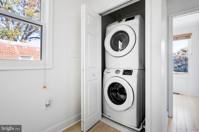 washroom featuring baseboards, laundry area, stacked washing maching and dryer, and light wood-style floors