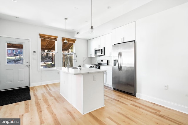 kitchen with a center island with sink, appliances with stainless steel finishes, decorative light fixtures, white cabinetry, and a sink