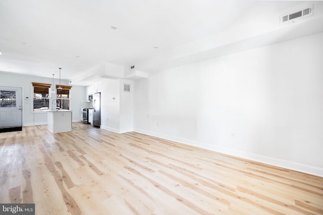 unfurnished living room featuring baseboards, light wood-style flooring, visible vents, and a sink