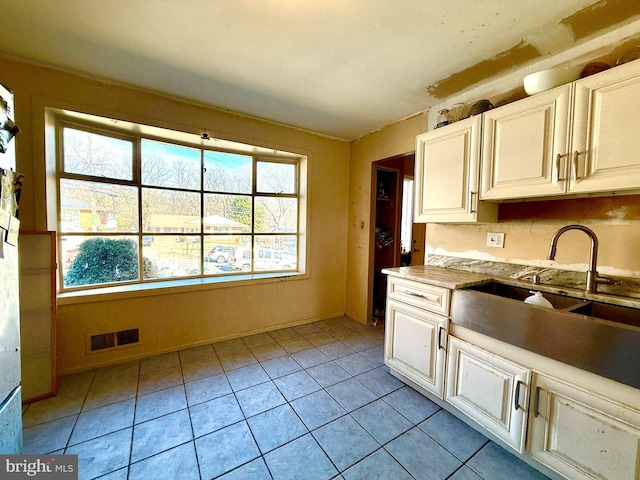 kitchen featuring light tile patterned floors, a sink, visible vents, and white cabinets