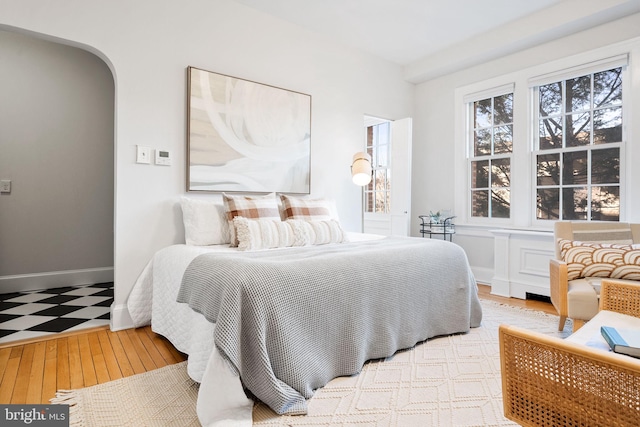 bedroom featuring baseboards, arched walkways, and wood finished floors