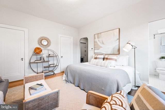 bedroom featuring arched walkways, baseboards, and wood finished floors