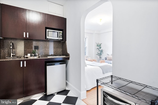 kitchen with arched walkways, decorative backsplash, dishwasher, stainless steel microwave, and light floors