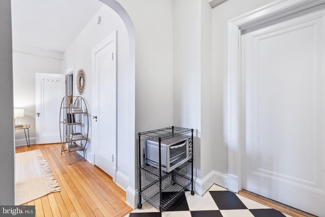 hall featuring light wood-type flooring, arched walkways, and baseboards