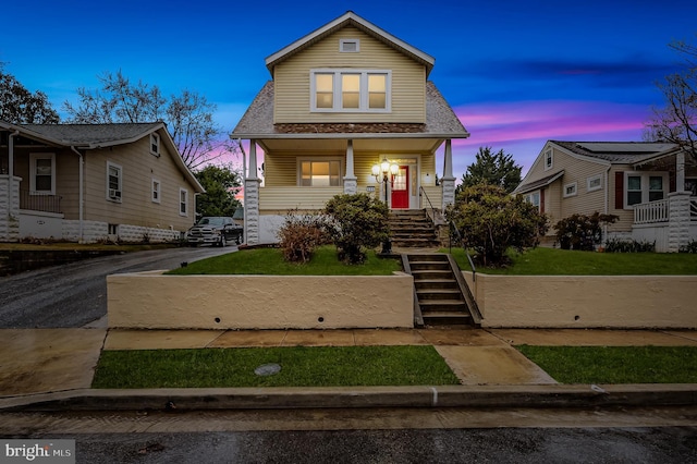 bungalow featuring covered porch, roof with shingles, a lawn, and stairway