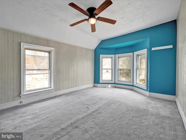 carpeted empty room with a ceiling fan, vaulted ceiling, a textured ceiling, and baseboards