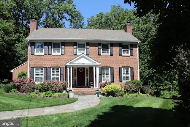 colonial-style house with brick siding, a chimney, and a front lawn