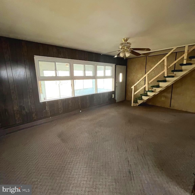 spare room featuring wood walls, ceiling fan, and stairway