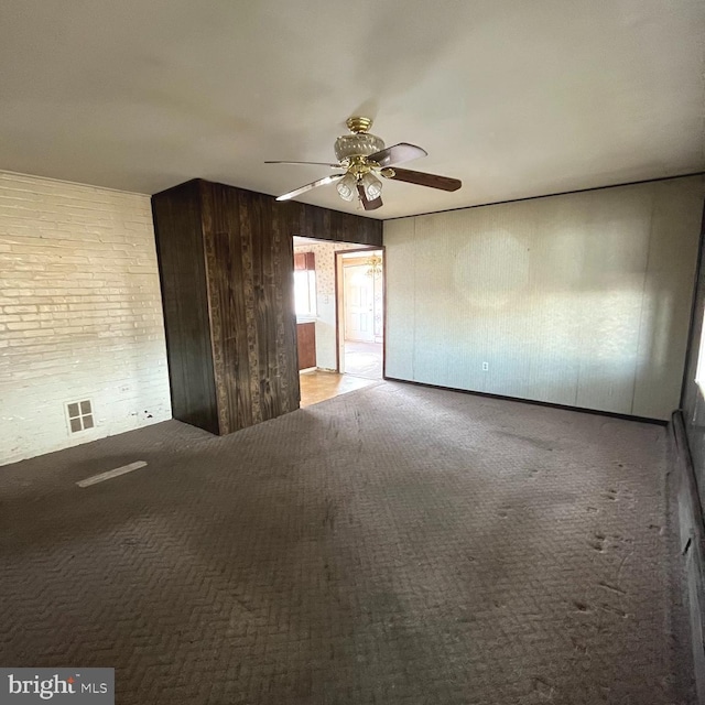 unfurnished room featuring ceiling fan, carpet flooring, visible vents, and wooden walls