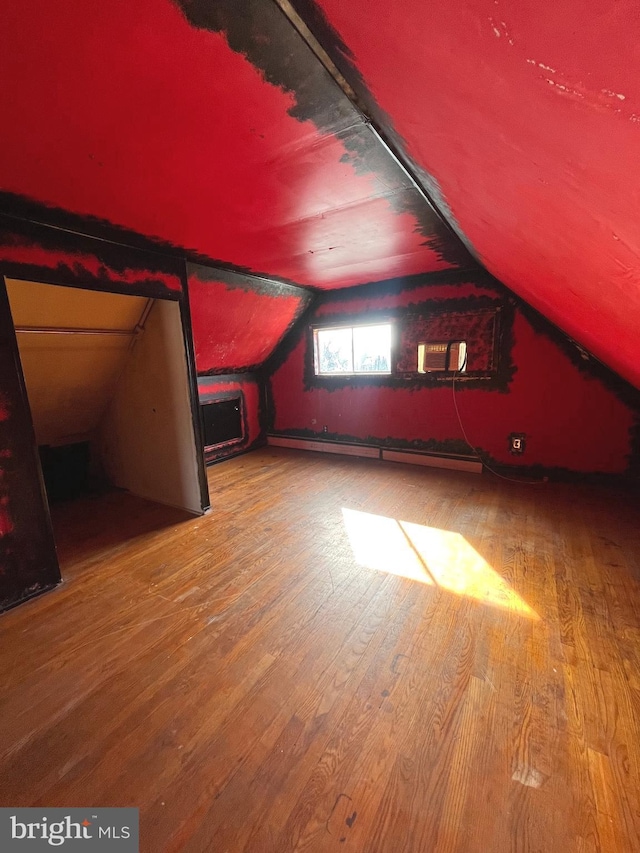 additional living space with lofted ceiling, a wall unit AC, wood finished floors, baseboard heating, and an AC wall unit