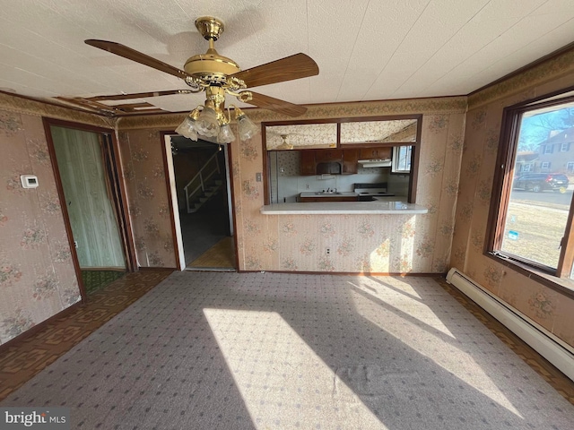 unfurnished living room featuring baseboard heating, plenty of natural light, a ceiling fan, and wallpapered walls