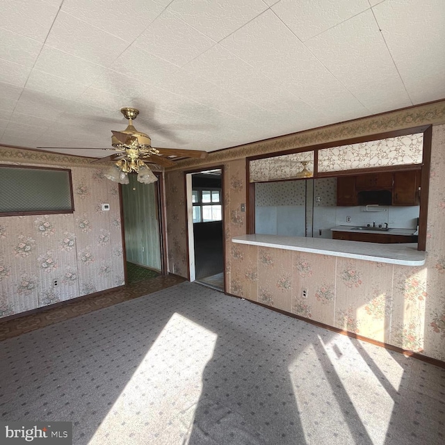 unfurnished living room featuring a ceiling fan and wallpapered walls