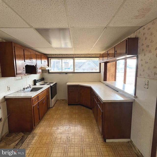 kitchen featuring white electric range oven, light floors, light countertops, under cabinet range hood, and a sink