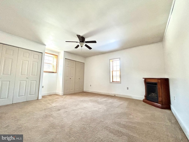 unfurnished living room featuring a wealth of natural light, light carpet, ceiling fan, and baseboards