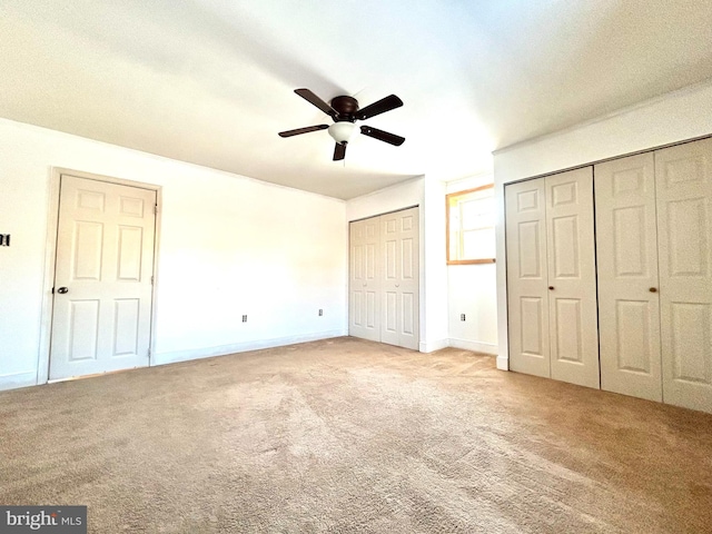 unfurnished bedroom with multiple closets, carpet flooring, baseboards, and a ceiling fan