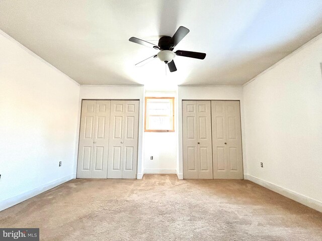 unfurnished bedroom with baseboards, two closets, and light colored carpet