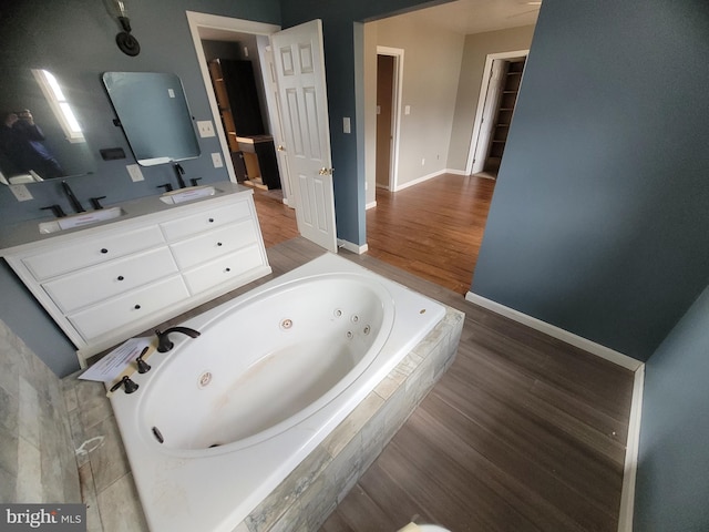 full bath with wood finished floors, a sink, baseboards, a whirlpool tub, and double vanity