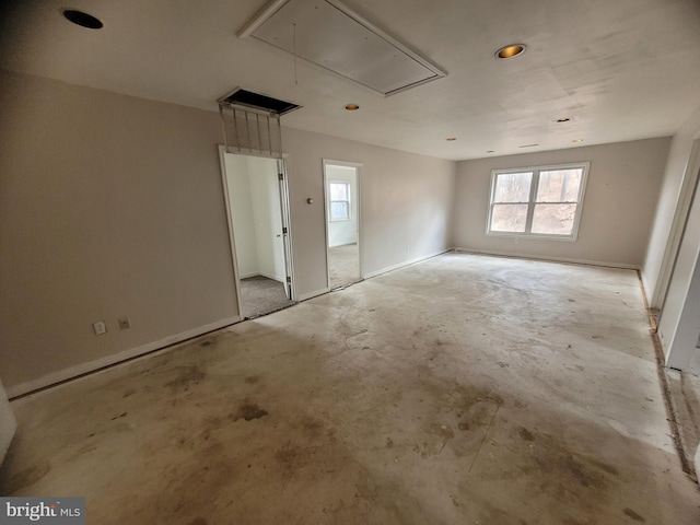 unfurnished bedroom featuring unfinished concrete flooring, attic access, and baseboards