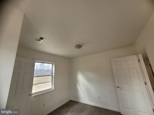 unfurnished room featuring dark carpet, visible vents, and baseboards