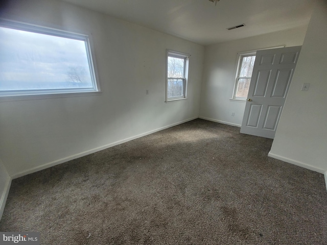 spare room featuring dark carpet, visible vents, and baseboards