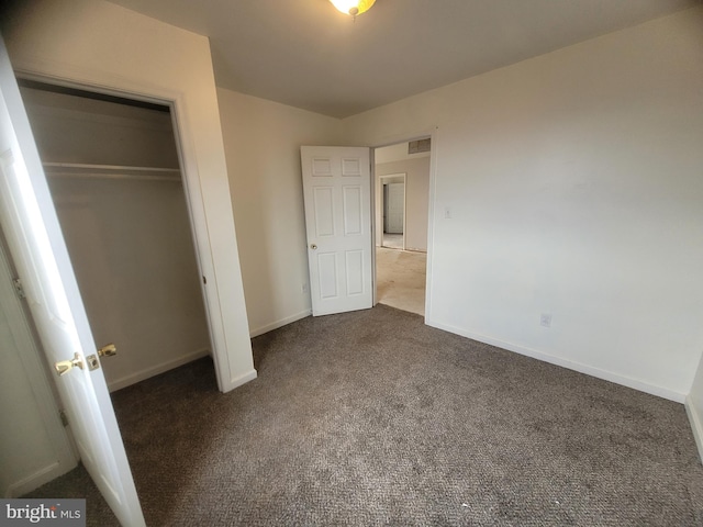 unfurnished bedroom with baseboards, visible vents, dark colored carpet, and a closet