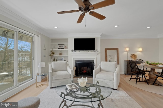 living room with built in features, a fireplace, crown molding, recessed lighting, and light wood-style flooring