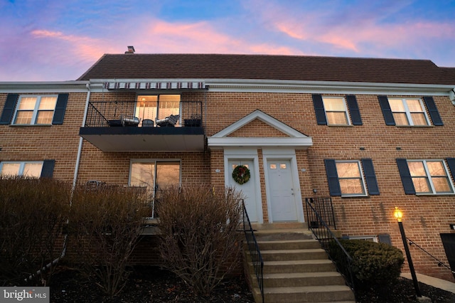 view of property featuring a shingled roof, brick siding, and a balcony