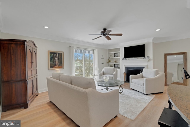 living area featuring ornamental molding, a fireplace, light wood finished floors, and ceiling fan