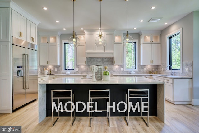 kitchen with built in refrigerator, visible vents, white cabinets, and a center island