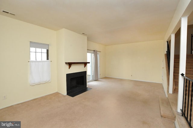 unfurnished living room featuring a fireplace with flush hearth, visible vents, and light colored carpet