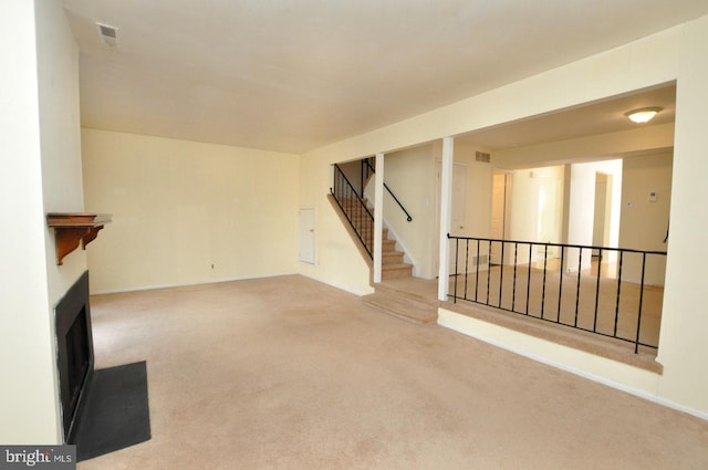 unfurnished living room featuring carpet, stairway, a fireplace, and visible vents