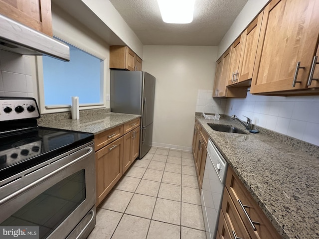 kitchen featuring light stone counters, stainless steel appliances, brown cabinetry, a sink, and under cabinet range hood