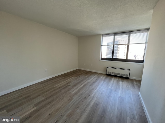 unfurnished room with a textured ceiling, wood finished floors, and baseboards