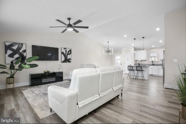 living area featuring lofted ceiling, recessed lighting, wood finished floors, baseboards, and ceiling fan with notable chandelier