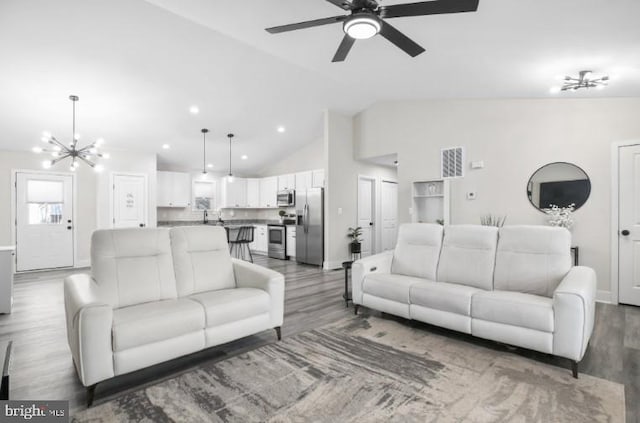 living room with ceiling fan with notable chandelier, baseboards, recessed lighting, and wood finished floors