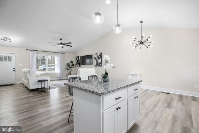 kitchen with light stone counters, a kitchen island, a kitchen breakfast bar, open floor plan, and light wood-type flooring