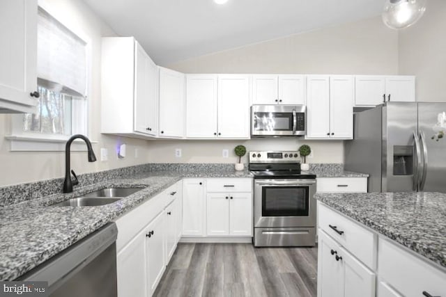 kitchen with appliances with stainless steel finishes, vaulted ceiling, white cabinets, and a sink