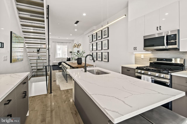 kitchen with wood finished floors, a center island with sink, a sink, decorative backsplash, and stainless steel appliances