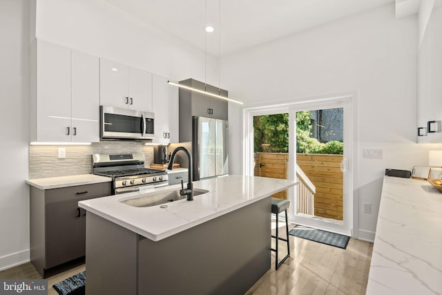 kitchen with a kitchen bar, a sink, tasteful backsplash, stainless steel appliances, and light wood finished floors