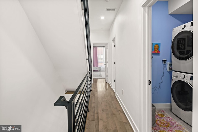 laundry area with visible vents, wood finished floors, stacked washing maching and dryer, baseboards, and laundry area