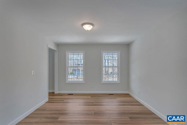 empty room with light wood-style floors, visible vents, and baseboards