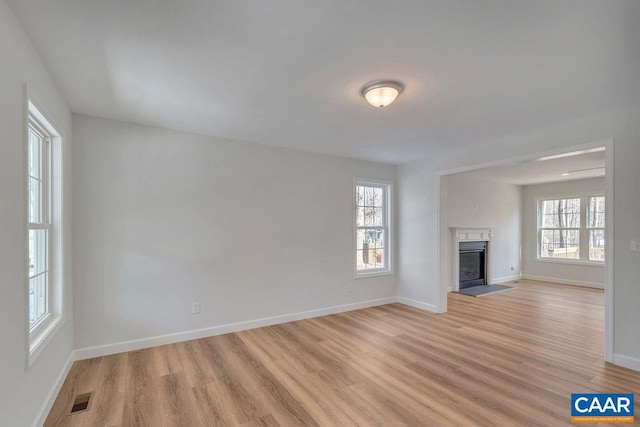 unfurnished living room featuring a fireplace with raised hearth, light wood finished floors, visible vents, and a healthy amount of sunlight