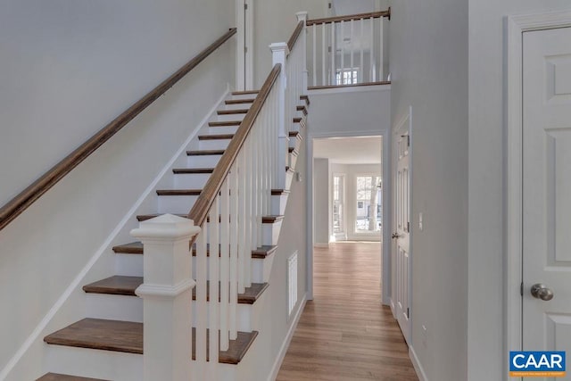 stairway featuring baseboards, a high ceiling, visible vents, and wood finished floors