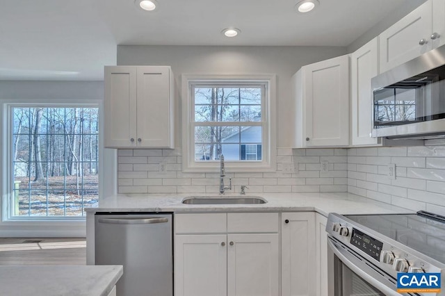 kitchen featuring appliances with stainless steel finishes, white cabinetry, a sink, and light stone countertops