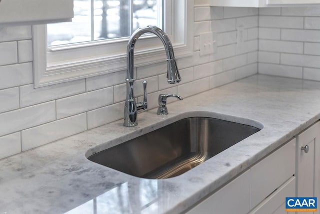 details featuring decorative backsplash, light stone counters, white cabinets, and a sink