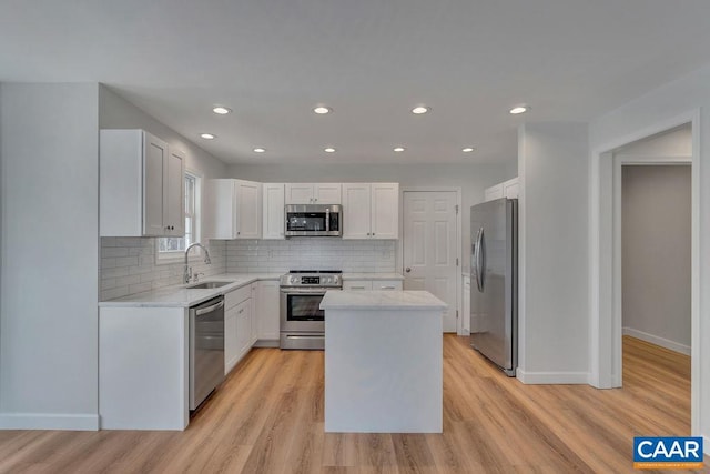 kitchen featuring stainless steel appliances, light wood-style flooring, white cabinets, a kitchen island, and a sink