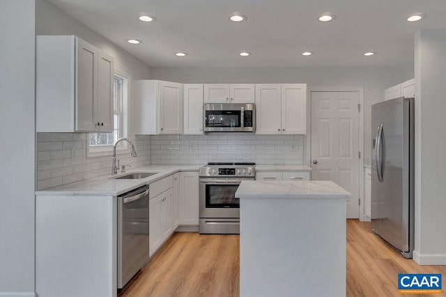 kitchen featuring stainless steel appliances, a kitchen island, a sink, white cabinetry, and light stone countertops