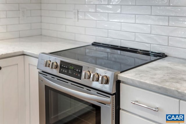 kitchen with tasteful backsplash, white cabinetry, stainless steel electric range oven, and light stone counters